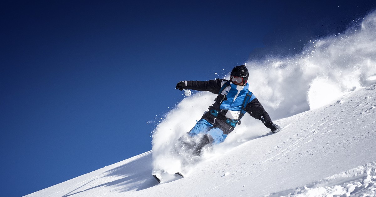 skier quickly descending on a snowy mountain with a clear blue sky behind