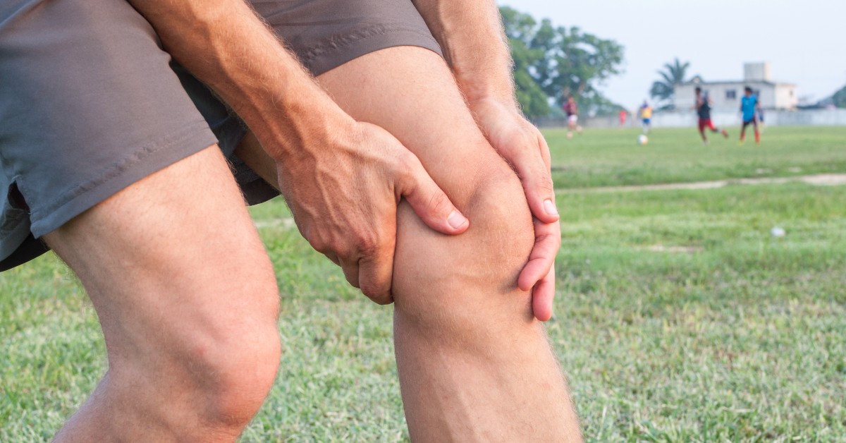 person in a grass field holding their left knee
