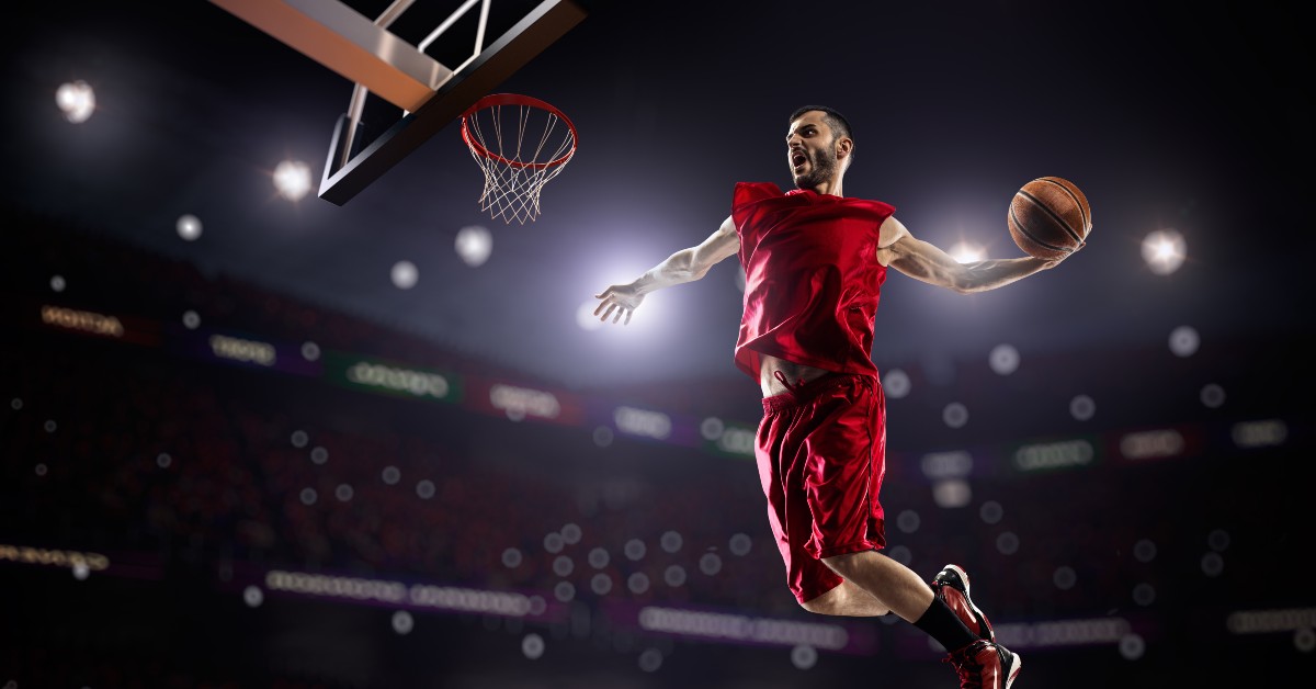 person in a basketball court jumping to the net with a ball in hand